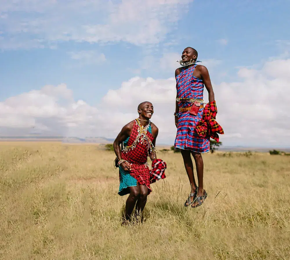 Two Maasai men in traditional dress jumping on the savannah