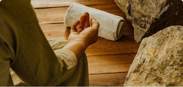 A hand resting in a meditation mudra on a wooden floor