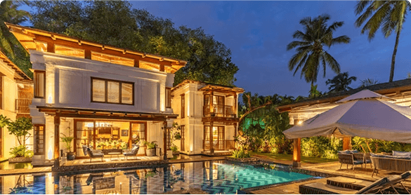 A lit villa beside a pool under palm trees at dusk