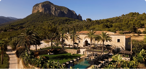 A stone finca with a pool beneath a rocky peak